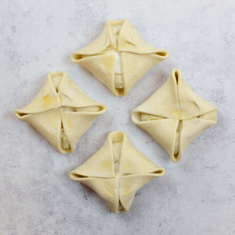 Four Goat Cheese Puff Pastry Baskets not yet baked placed in a diamond pattern on marble, seen from above. 