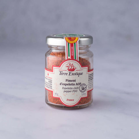 Glass jar containing Espelette Chili Pepper PDO spices from the Terre Exotique brand, front view.