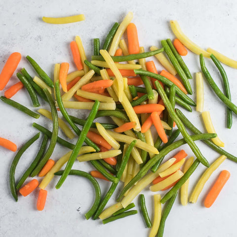 Assortment of vegetables including tender haricot verts, vibrant yellow wax beans, and sweet young baby carrots, scattered on marble, seen from above.