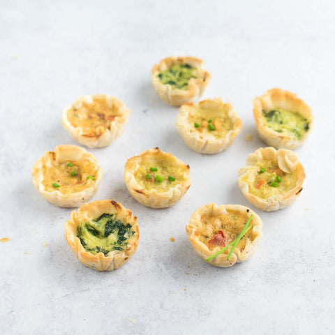 Assortment of 9 Mediterranean-Style Fillo Quiches, arranged on marble, front view. 