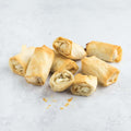 Assortment of Goat Cheese and Fig Fillo Rolls arranged on marble, seen from front. 