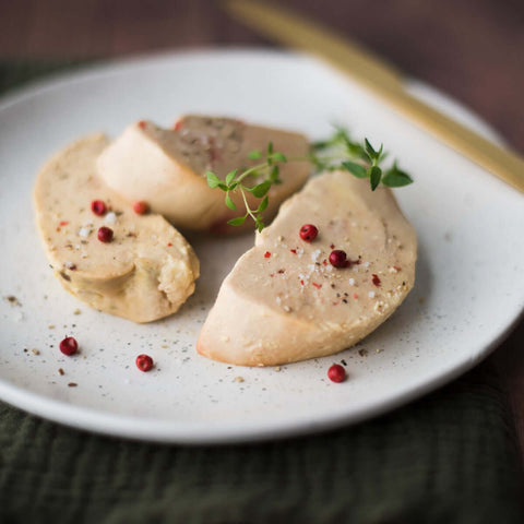 3 slices of Foie Gras arranged in a round plate with pink peppercorns, seen from above. 