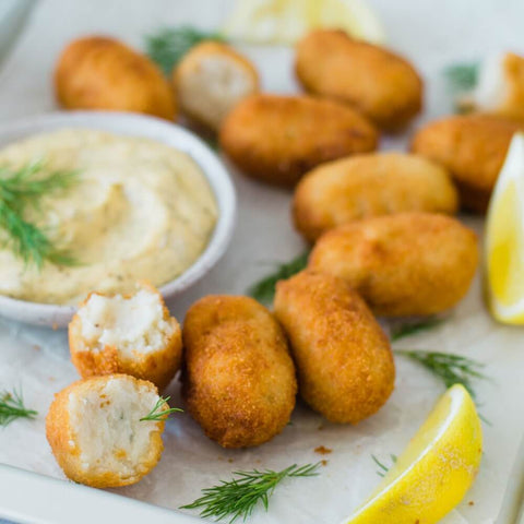 Assorted Cod Croquettes cooked, laid with some thyme branches, lemon and a jar of sauce, front view.