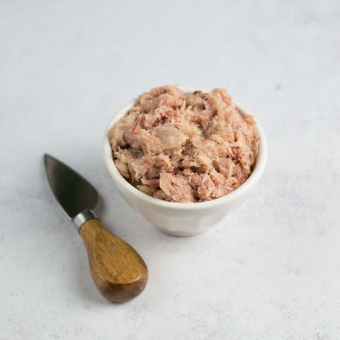 Rillette du Mans in a bowl set on marble, with a knife to the left of the bowl, seen from the front. 