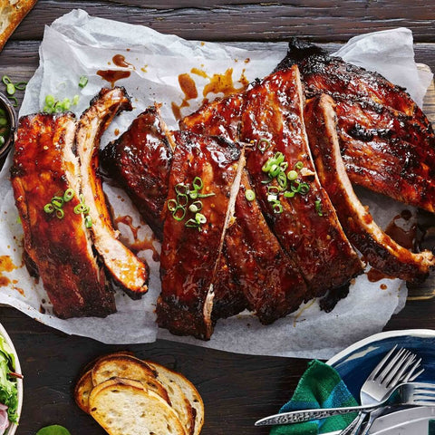 Marinated and cooked Ib??rico Pork Spare Ribs, sliced on a sheet of baking paper, with a few slices of bread, seen from above. 