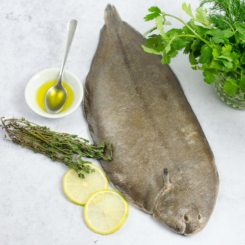 French Dover Whole Sole arranged on marble with chives, thyme, lemon and a small bowl of olive oil, seen from above. 