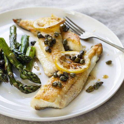 French Dover Whole Sole cooked and arranged in a round plate with vegetables and lemon, seen from above. 