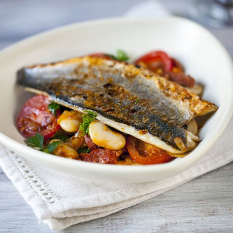 Piece of Estuary Branzino - European Seabass (Skin-On) cooked in a round plate with tomatoes and basil, side view