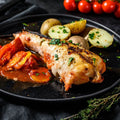 Piece of wild monkfish cooked in a round plate with potatoes and tomatoes, seen from the side.