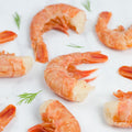 Assortment of 8 Ez-Peel Shrimp arranged on marble with some leaves of chives, front view.