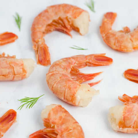 Assortment of 8 Ez-Peel Shrimp arranged on marble with some leaves of chives, front view.