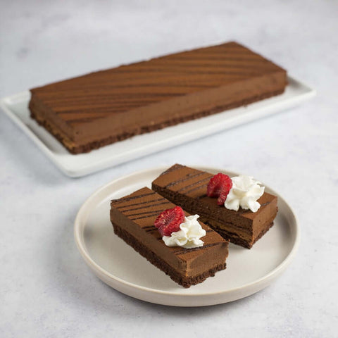 A large Crunchy Chocolate Hazelnut Strip Cake placed in a tray and two small pieces of Crunchy Chocolate Hazelnut Strip Cake placed in a round plate, seen from the front. 