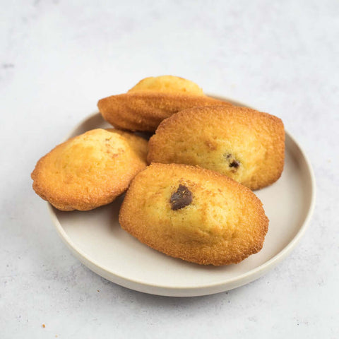 Assortment of 4 Chocolatey Hazelnut Filled Madeleines arranged on a round plate, top view. 