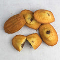 Assorted Chocolatey Hazelnut Filled Madeleines with one cut in half, arranged on marble, seen above. 