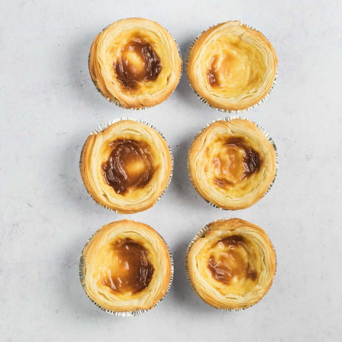 Assortment of 6 Pastéis de Nata placed on marble, seen from above.