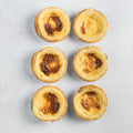 Assortment of 6 Past??is de Nata placed on marble, seen from above.