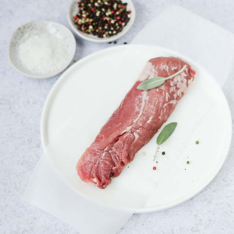 Iberico Pork Tenderloin placed in a round plate, with some black peppercorns and salt, seen from above. 