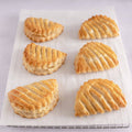 6 Apple turnovers from At Home French Bakery placed on a grid with baking paper, front view.
