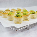 Assortment of 16 Mini Vol Au Vent not yet cooked, placed on a plate and baking paper, side view.